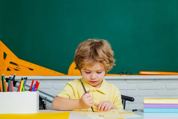 Zpátky do školy. Šťastně se usmívající žák kreslí za stolem. Roztomilý malý školáček s učitelským studiem ve třídě. Základní škola a vzdělávání. — Stock fotografie
