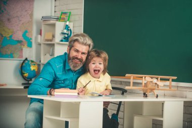 Okul malzemeleriyle masasının yanında gülen surat ifadesi olan küçük bir çocuk. Okuldan sonra. İlkokul öğretmenliği.