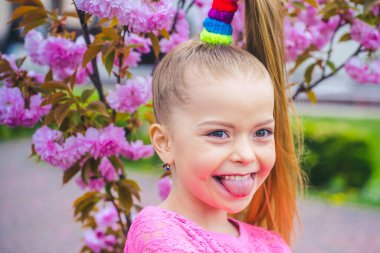 Küçük mutlu kız pembe çiçeklerle kiraz ağacının altında oynuyor. Komik surat..