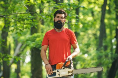 Ormanın yakınında baltası olan yakışıklı bir genç. Oduncu konsepti. Tarım ve ormancılık teması. Ormanların yok edilmesi. Yenilenebilir enerji kaynağı olarak yakacak odun.