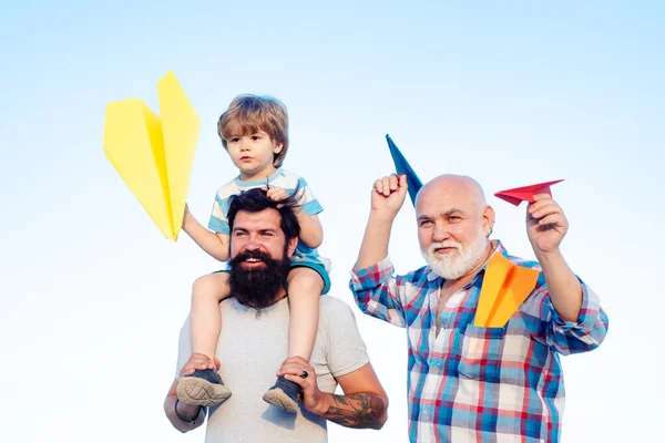 Szczęśliwe dziecko bawiące się zabawkowym papierowym samolotem na tle letniego nieba. Ojciec syn i dziadek relaksują się razem. mężczyzna wielopokoleniowa rodzina. — Zdjęcie stockowe