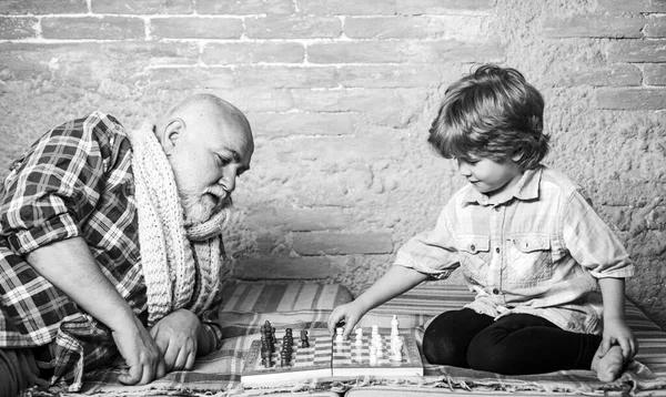 老人は孫にチェスを教える。ハンサムなおじいちゃんと孫は家で一緒に時間を過ごしながらチェスをしています. — ストック写真