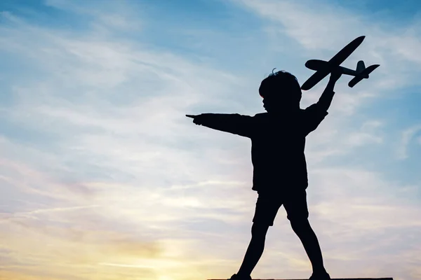 Silhouette of child with airplane in sunlight rays. Concept of dreams and travels. Dreams of flying planes. — Stock Photo, Image