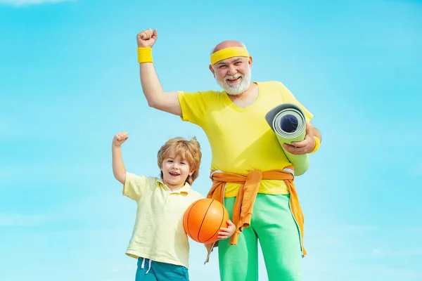 Uomo anziano e bambino che si esercitano sul cielo blu. Sport per bambini. Sportivo nonno e sano bambino con pallone da basket su sfondo cielo blu . — Foto Stock