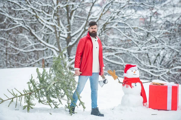 Bûcheron hipster avec sapin de Noël. Coupe-bois avec hache dans la forêt d'hiver. Homme barbu avec arbre de Noël fraîchement coupé en forêt . — Photo