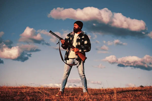 Bearded hunter man holding gun and walking in forest. Hunter with shotgun gun on hunt.