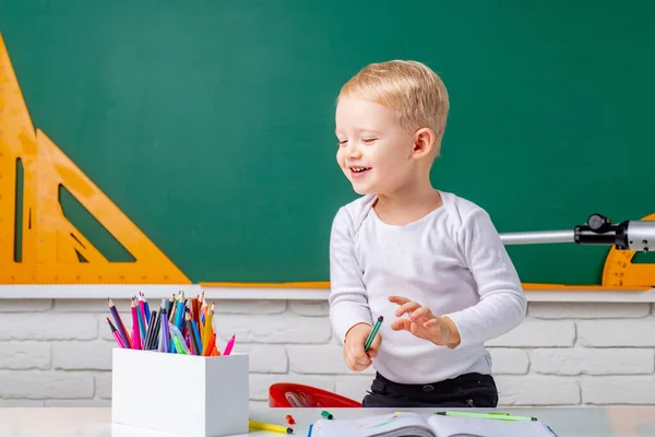 Szczęśliwe słodkie pracowite dziecko siedzi przy biurku w domu. Indywidualne nauczanie. Portret ucznia w szkole podstawowej w pomieszczeniach. — Zdjęcie stockowe