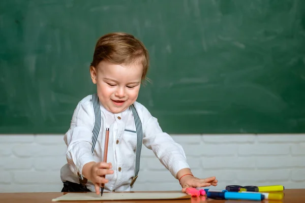 Proceso educativo en preescolar. Preescolar en el aula cerca del escritorio de pizarra . — Foto de Stock