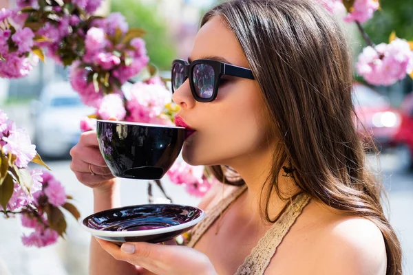 Primer plano retrato de hermosa chica sostener taza de cofee con matcha. Buenos días. Fondo cálido de la flor de primavera. Bebida de moda latte matcha o mocha . —  Fotos de Stock