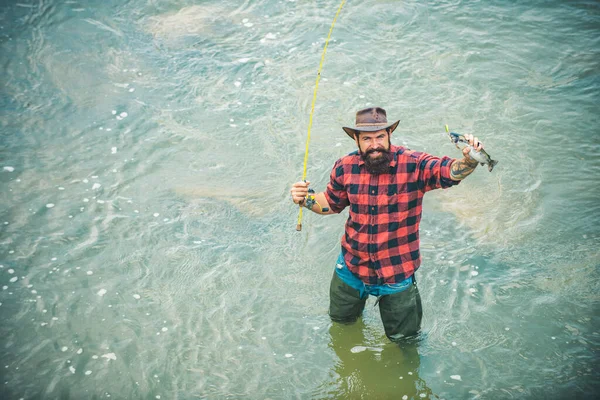 Fishernek van hala és hosszú botja. Az ember pihen és horgászik a folyón. Boldog szakállas halász a vízben. Jól érzem magam. Aktív napsütéses nap. Hobbi és sport tevékenység. Férfi hobbi. — Stock Fotó