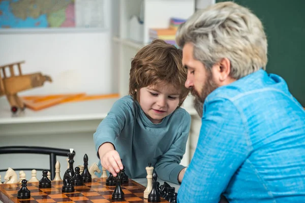 Handsome teacher giving private lessons chess to preschool boy. Father teaching his son to play chess. Intelligent kids.