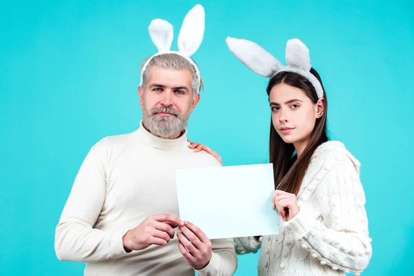 Glad påskfamilj. Lustigt kaninpar håller pappret. Pojke och flicka i kostym påsk kanin på blå bakgrund isolerad. — Stockfoto
