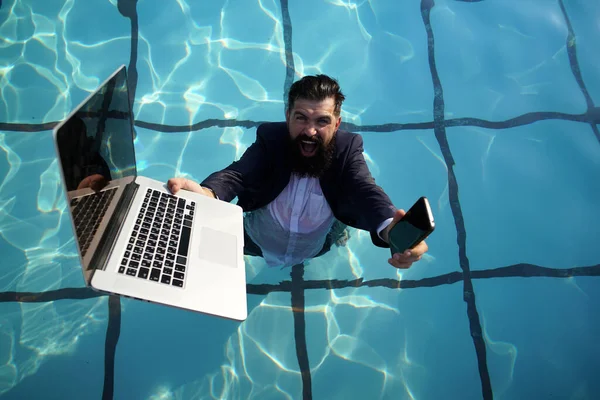 Business man in suit with a laptop in one hand and a mobile phone in another in Pool. Freelancer working on vacation next to the swimming pool. — Stock Photo, Image