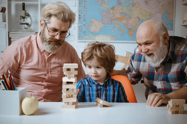 祖父、父と息子は自宅でjengaゲームをプレイ。笑顔の祖父、父と就学前の息子の頭のショット肖像画. — ストック写真
