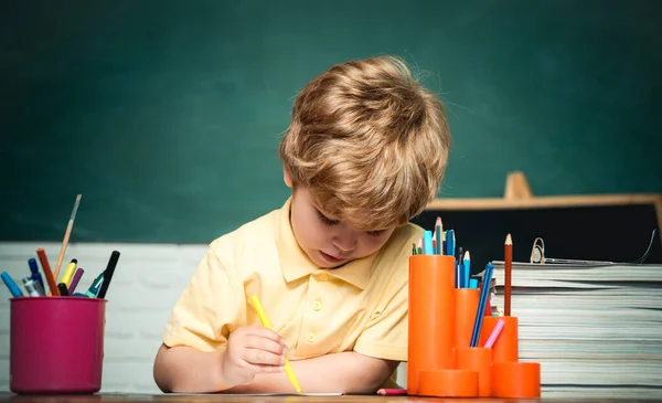 Concetto scolastico. Lavagna copiare spazio - concetto di scuola. Spazio copia lavagna. Felice bambino carino laborioso è seduto a una scrivania al chiuso — Foto Stock