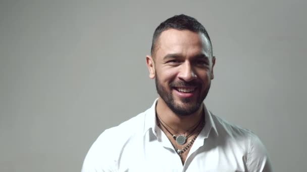 Hombre sonriente sobre fondo gris. Las emociones del hombre. Retrato del hombre sonriente de cerca. Exitoso modelo hispano masculino. Guapo hombre sonriente sobre fondo gris mirando a la cámara. Feliz sonrisa retrato . — Vídeo de stock