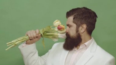 Bir buket çiçeğin arkasına saklanan bir adam. Teklif sahnesi. Düşünen şık genç adamın portresi başka tarafa bakıyor. Elinde bir buket kırmızı gül tutan yakışıklı adam, yeşil üzerine izole edilmiş..