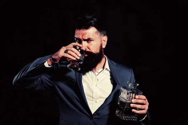 Man or businessman drinks whiskey on black background. Cheerful bearded man is drinking expensive whisky.