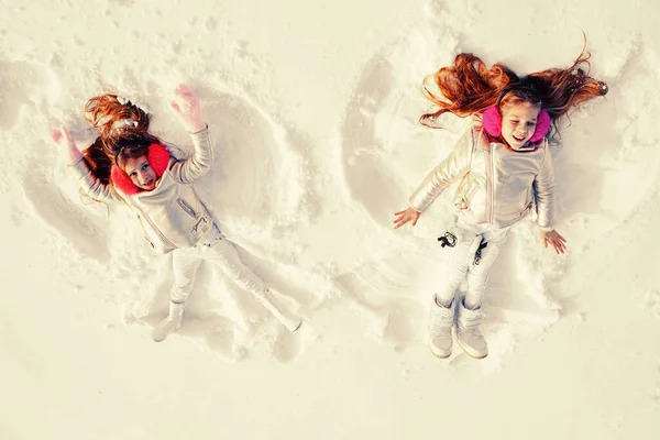 Snow angels made by a kids in the snow. Smiling children lying on snow with copy space. Funny kids making snow angel. Top view.