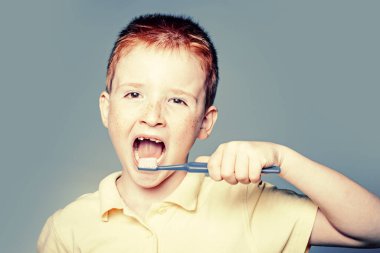 Çocuk dişlerini fırçalıyor. Dişlerini fırçalayan mutlu çocuk. Mavi arka planda diş fırçası olan tek dişli gülen çocuk. Gömlek tasarımı, sağlık, ağız temizliği..