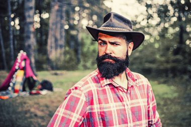 Ormandaki adam. Yakışıklı sakallı erkek. Doğal arka plan. Ağaçların arka planında şapkalı, esmer ve sakallı vahşi bir adam. Sakallı, olgun bir hippi. Vahşi sakallı adam..