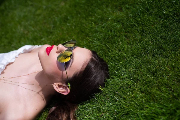 Glad ung kvinna i snygga kläder ligger på en grön, vacker gräsmatta. Vår flicka ligger på gräset. — Stockfoto