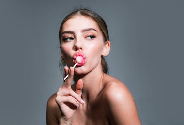 Şeker yalayan kız. Lolipop modeli. Kadın dudakları şeker emiyor. Gri arka planda dudaklarından lolipop emen bir kadın. Glamor güzel genç kadın model kırmızı dudaklı Eşofman altı yiyor lolipop.