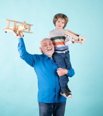 Gelecek nesil aile rüyası. Mavi arka planda oyuncak uçağı olan mutlu büyükbaba ve torun izole edildi. Mutlu büyükbaba, torununu sırtında taşıyor..