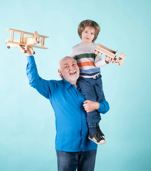 家庭世代的未来梦想。快乐的祖父和孙子与玩具飞机与蓝色背景隔离。爷爷很高兴让孙子骑在肩上. — 图库照片