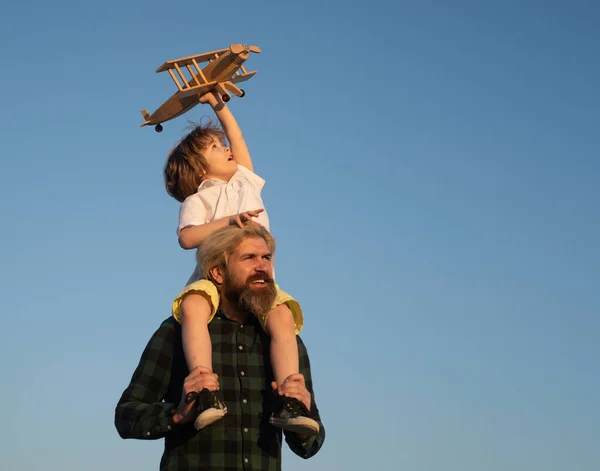 Padre e hijo. Niño con avión de juguete sentado en los hombros de los padres. Feliz momento de padre hijo. padre piggybacking su chico en el cielo mientras es jugando con juguete avión . — Foto de Stock