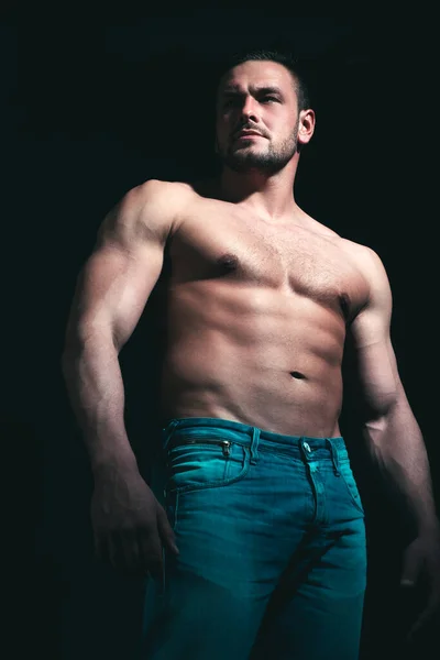 Hombre musculoso fuerte y serio. Hombre fuerte sexual guapo con cuerpo muscular en jeans posando en estudio sobre fondo negro . — Foto de Stock