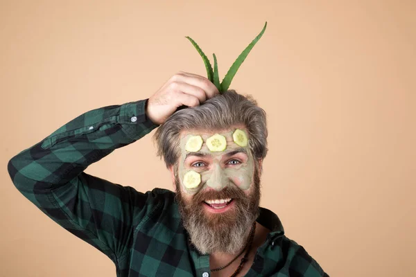 Salatalıklı ve aloe veralı eğlenceli yüz maskeli bir adam eğleniyor. Spa adamı yüz kilinden maske takıyor.. — Stok fotoğraf
