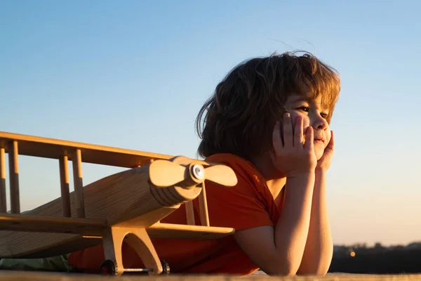 Dítě si při západu slunce hraje s letadýlkem. Snový chlapec s dřevěným letadlem. Dětský pilot letec s letadlem sny o cestování. — Stock fotografie