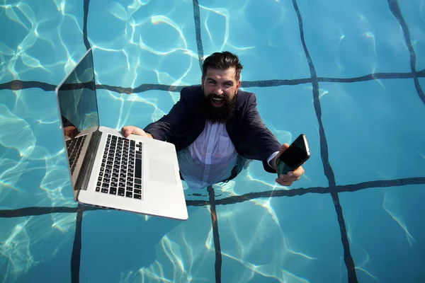 Funny bearded business man in suit using phone and laptop in swimming pool. Concept of young people working mobile devices. — Stock Photo, Image