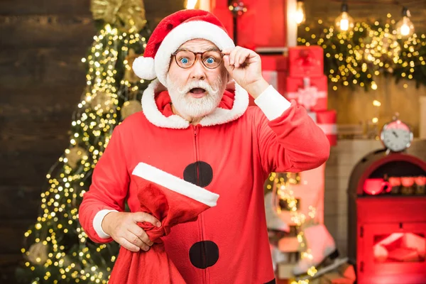 Babbo Natale con regali regalo. Babbo Natale a casa con la borsa di Natale. Uomo barbuto divertirsi vicino all'albero di Natale al chiuso . — Foto Stock