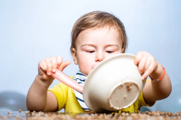 Lyckligt barn med en sked. Babyätande. Grabben leker i köket med disken. Lycklig pojke sked äter sig själv. — Stockfoto