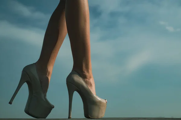 穿着高跟鞋的年轻女子的腿的特写。美丽的女性腿，脚跟在天空的背景。高跟鞋中的女性细腿. — 图库照片