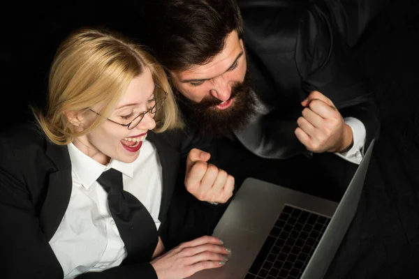 Couple being happy winning a bet in online sport gambling application on his notebook. Excited Business people with laptop on black background isolated. Young couple is working on laptop and smiling.