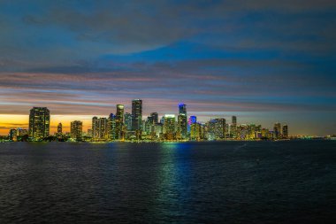 Miami Florida, HDR. Alacakaranlıkta Miami City gökdelenleri ve deniz üzerindeki yansımalı köprü ile gökyüzü manzarası.