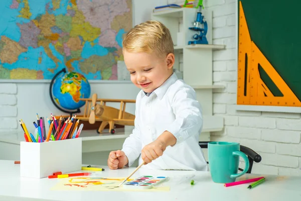 Niño amable en el aula cerca del escritorio de pizarra. Niños pequeños en la escuela. El niño está aprendiendo en clase en el fondo de la pizarra . — Foto de Stock