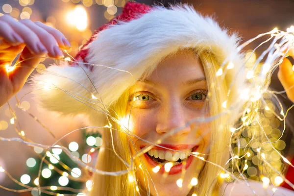 Gülümseyen kadın. Noel ışığı. Noel Baba kıyafetleri giymiş güzel bir kızın portresi. Kırmızı Noel Baba şapkalı kadın Noel ışığı tutuyor.. — Stok fotoğraf
