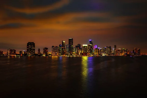 Miami belvárosa éjjel. Miami város, Florida felhőkarcoló panoráma alkonyatkor városi felhőkarcolókkal és a tenger feletti híd elmélkedéssel. Miami Florida, a belvárosi éjszakai színes felhőkarcoló — Stock Fotó