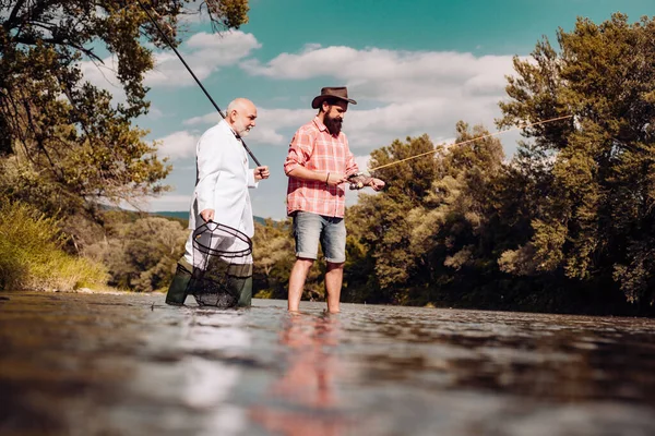 Elegante uomo barbuto e brutale pesca hipster. Hobby attività sportive. Padrone Baiter. Padre e figlio adulto pesca sul lago. Amici uomini con canna da pesca e rete. Pescatore barbuto in pensione . — Foto Stock