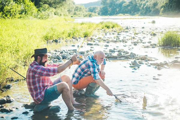 Two fishermen relaxing together while fishing on the lake at the morning. Retired dad and mature bearded son. I am happiest man. Two male friends fishing together. Men fishing on the lake. — Stock Photo, Image