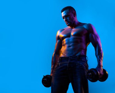 Güçlü adam mavi arka planda dambıllarla çalışıyor. Adam dambılları kaldırıyor. Kuvvet ve motivasyon.