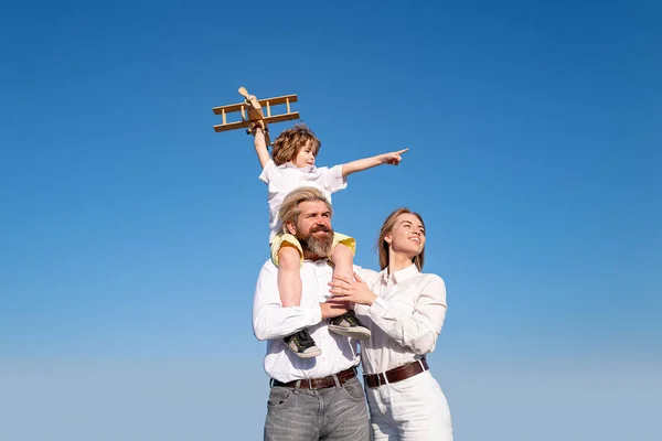 Famille heureuse : mère père et enfant fils rêvant de voyager en famille. Profiter de la vie ensemble. Concept de voyage en famille de vacances. Garçon avec jouet avion assis sur les épaules des pères . — Photo