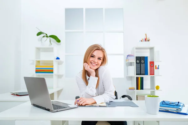Giovane donna d'affari sorridente in ufficio moderno bianco. Segretaria di bellezza. Bella giovane donna che lavora con il computer portatile in ufficio . — Foto Stock