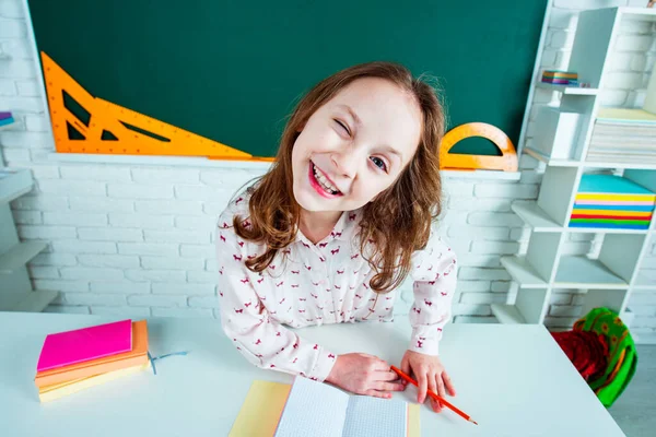 Imparare i bambini. Ragazza divertente bambino in classe vicino alla scrivania della lavagna. Istruzione scolastica e concetto di persone - allievo carino su sfondo lavagna . — Foto Stock