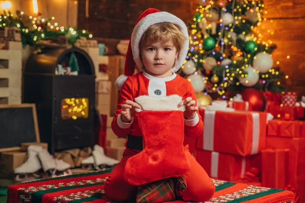 クリスマスのストッキング、靴下にクリスマスプレゼントの小さな男の子。新年明けましておめでとう。屋内だ。メリーと明るいクリスマス。子供の頃の記憶。新年。素敵な赤ちゃんは休日を楽しむ. — ストック写真