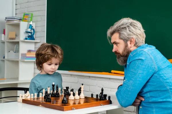 Tuteur à domicile aidant garçon avec des études d'échecs. Joyeux petit enfant jouant aux échecs avec un homme âgé à la maison . — Photo